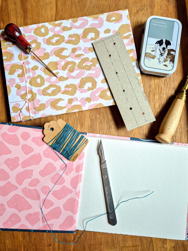 An image of a table with 2 books on it, one lying open, the other closed. There are various bookbinding tools on the table also.